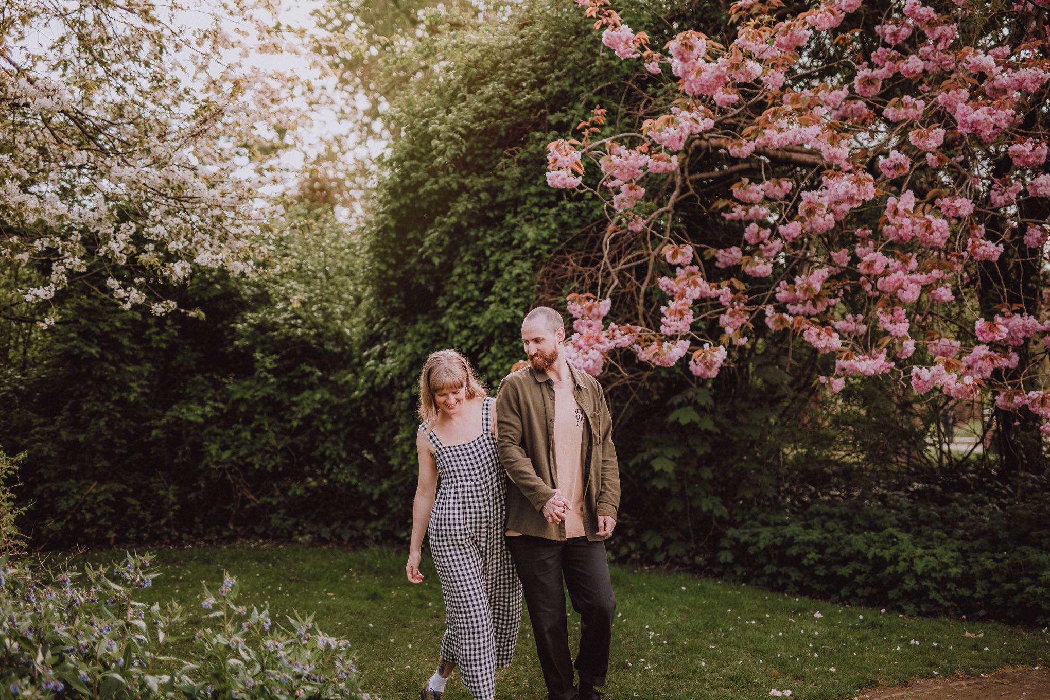 Candid engagement photography of a couple strolling beneath blossoming trees in a garden setting, unposed and intimate moment full of calm and warmth, relax natural wedding photographer Glasgow Scotland