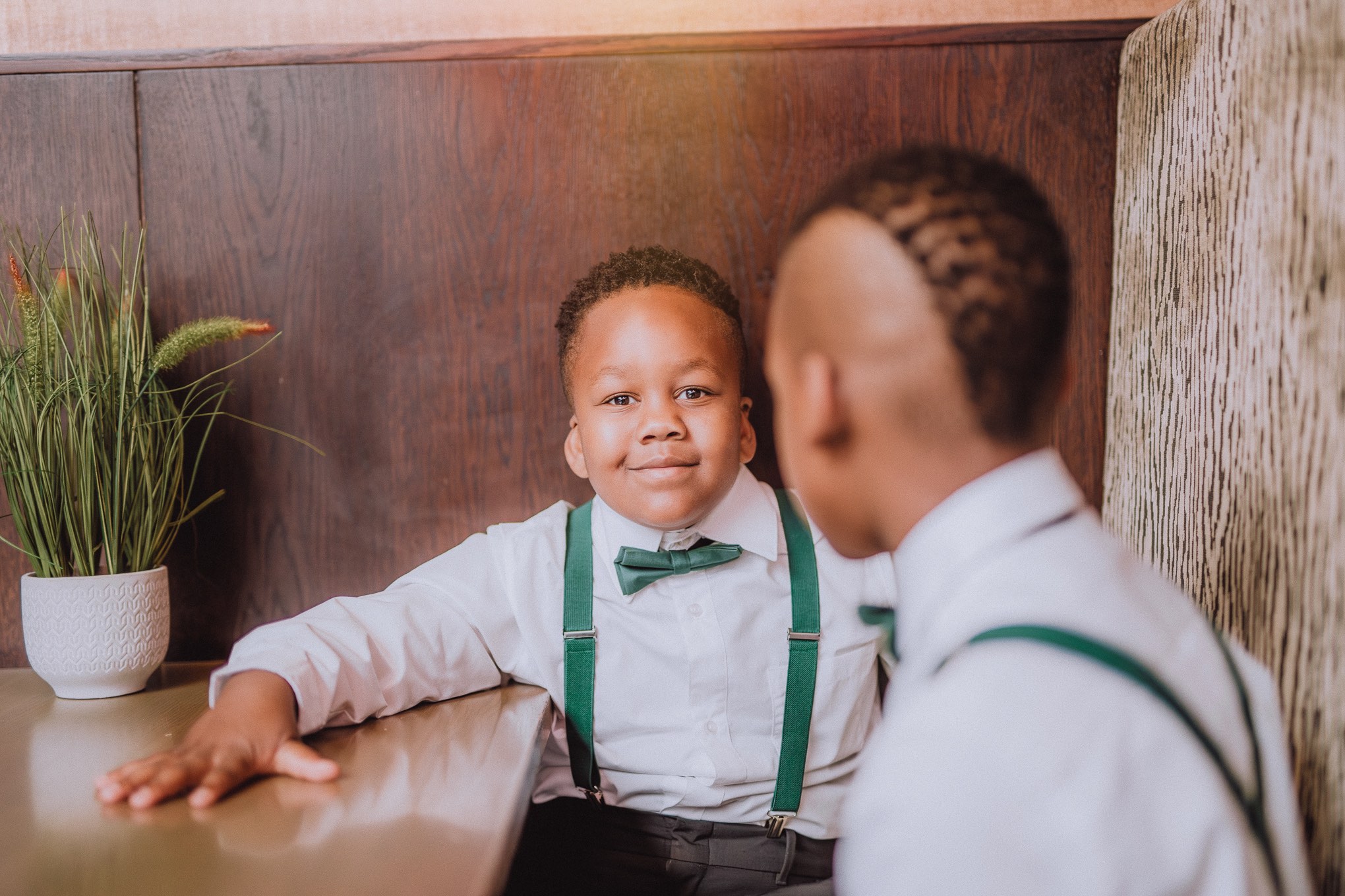 Young page boy wearing green suspenders and a bow tie, smiling during a quiet moment indoors before a wedding ceremony, relax natural wedding photographer Glasgow Scotland