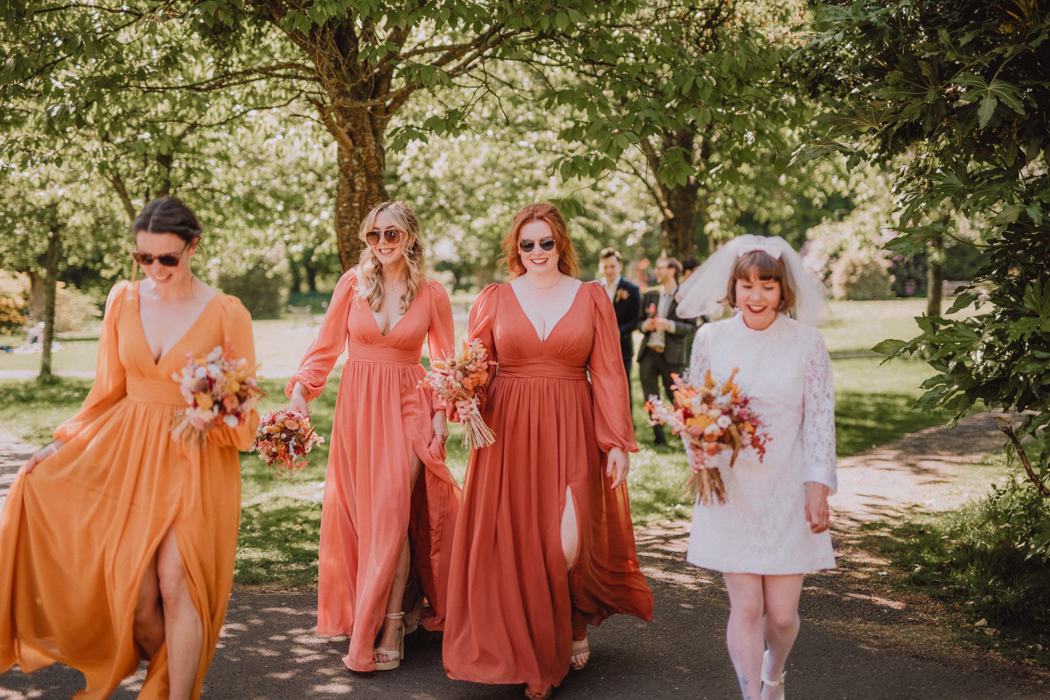 Bride walking alongside her bridesmaids through sunlit gardens, dresses flowing and laughter shared during a relaxed outdoor wedding moment in Scotland, relaxed natural waiting photography Scotland