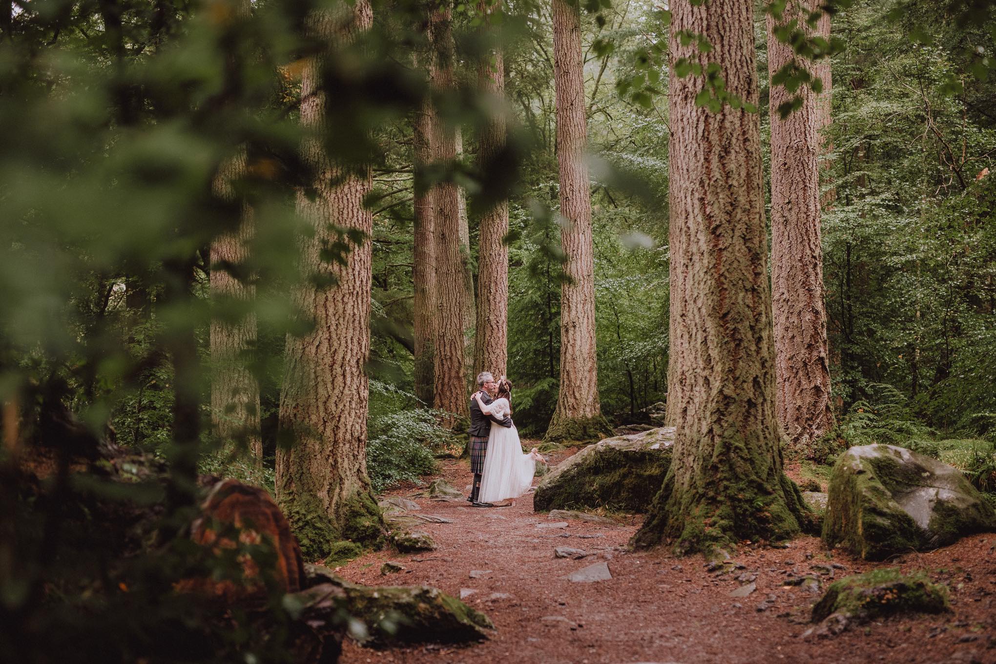 Intimate portrait of a couple embracing on a woodland path surrounded by tall trees, quiet moment captured deep in nature, relax natural wedding photographer Glasgow Scotland