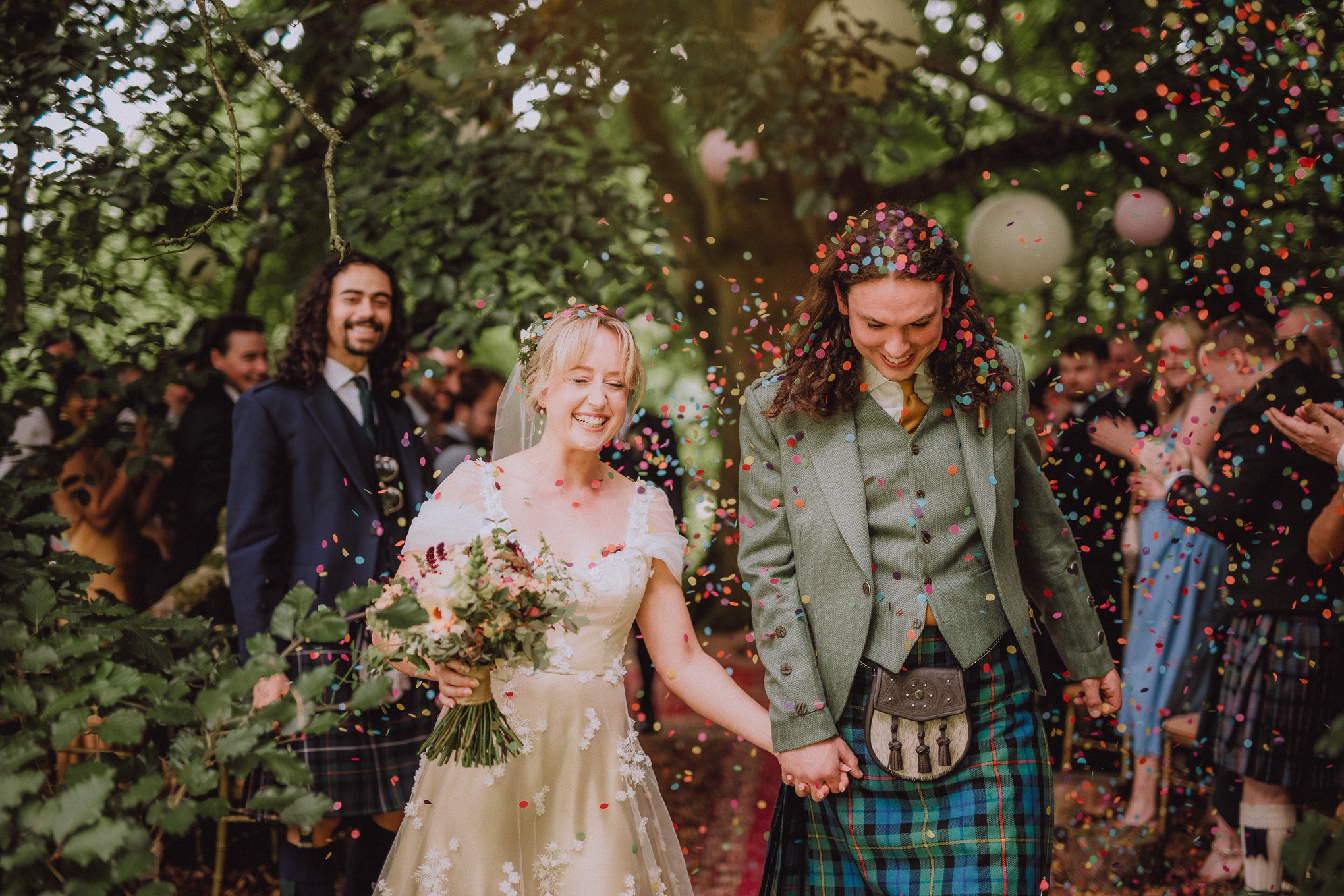 Newly married couple walking hand in hand through falling confetti during an outdoor ceremony, photographed in a relaxed natural wedding photography Scotland style