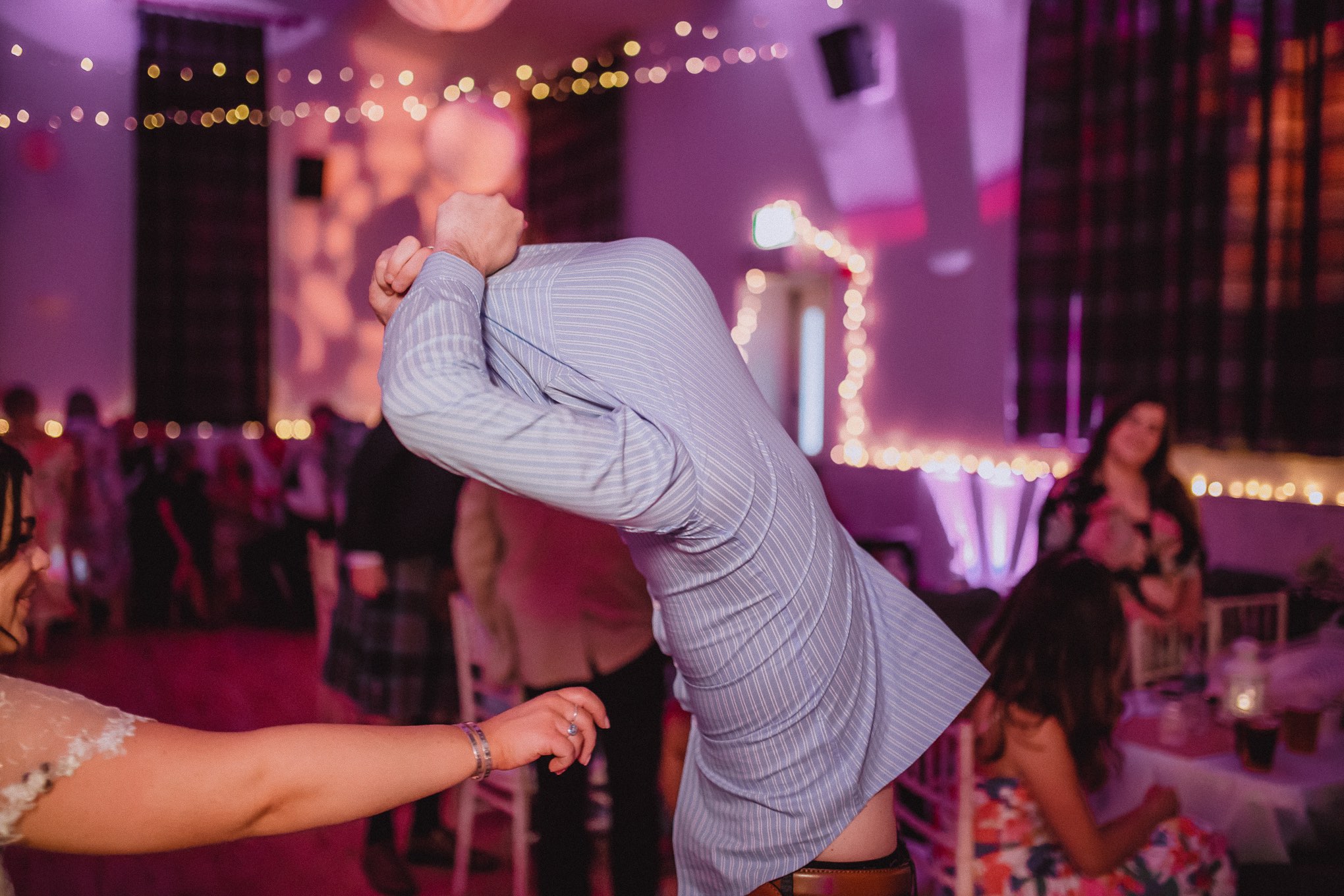 Wedding guest dancing wildly on the dance floor during the evening reception, arms raised under colourful party lights and blurred motion, relax natural wedding photographer Glasgow Scotland