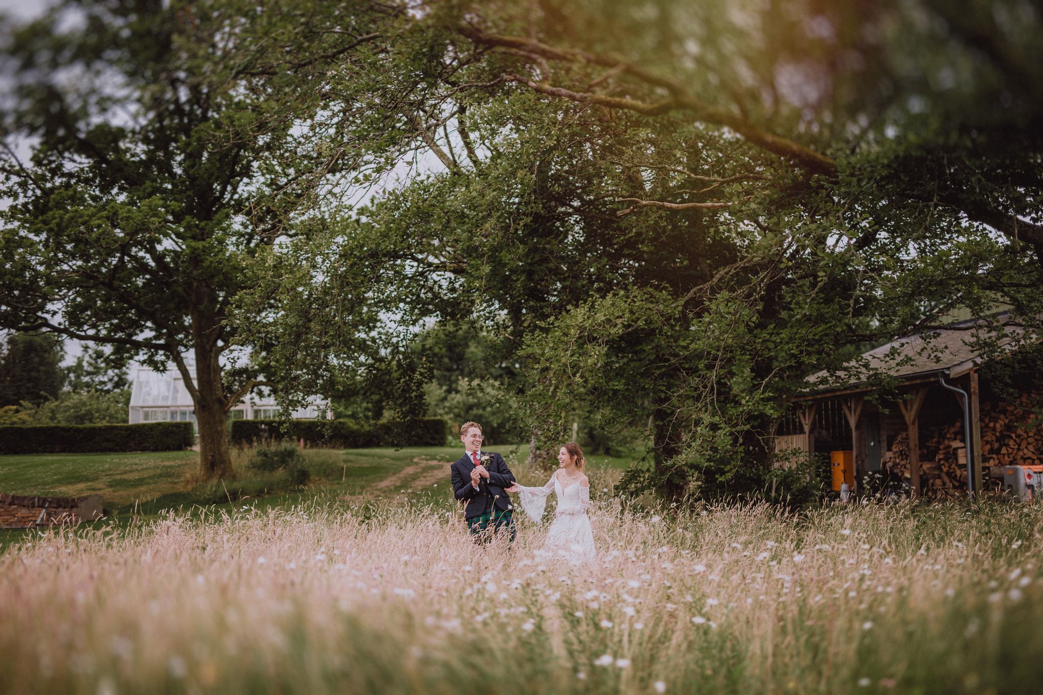Newly married couple running hand in hand through long grass in a rural setting, wide scenic shot capturing freedom and movement, relax natural wedding photographer Glasgow Scotland