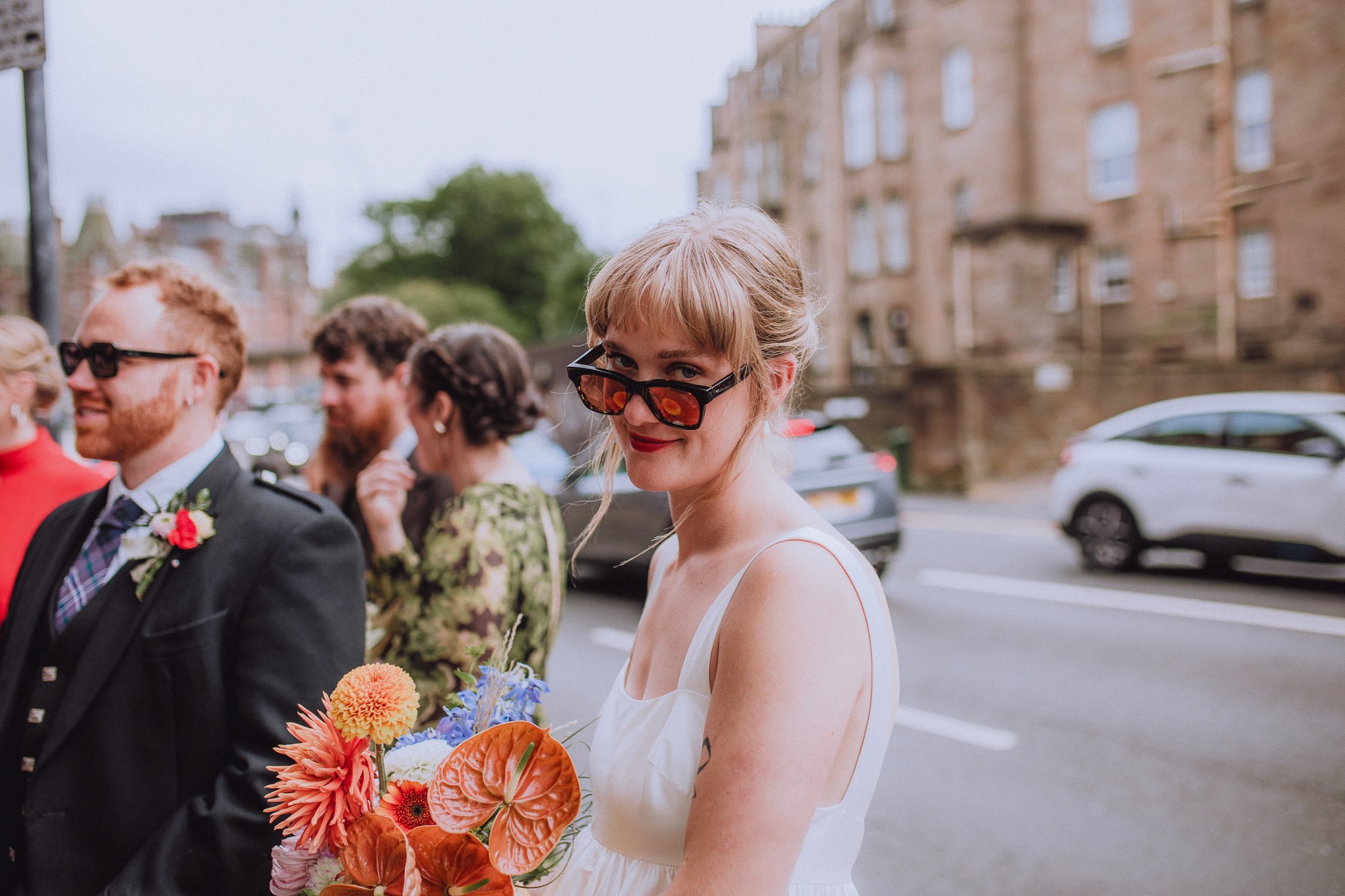 Bride holding a vibrant bouquet while standing casually with wedding guests on a Glasgow street, relaxed urban wedding moment full of character, relax natural wedding photographer Glasgow Scotland